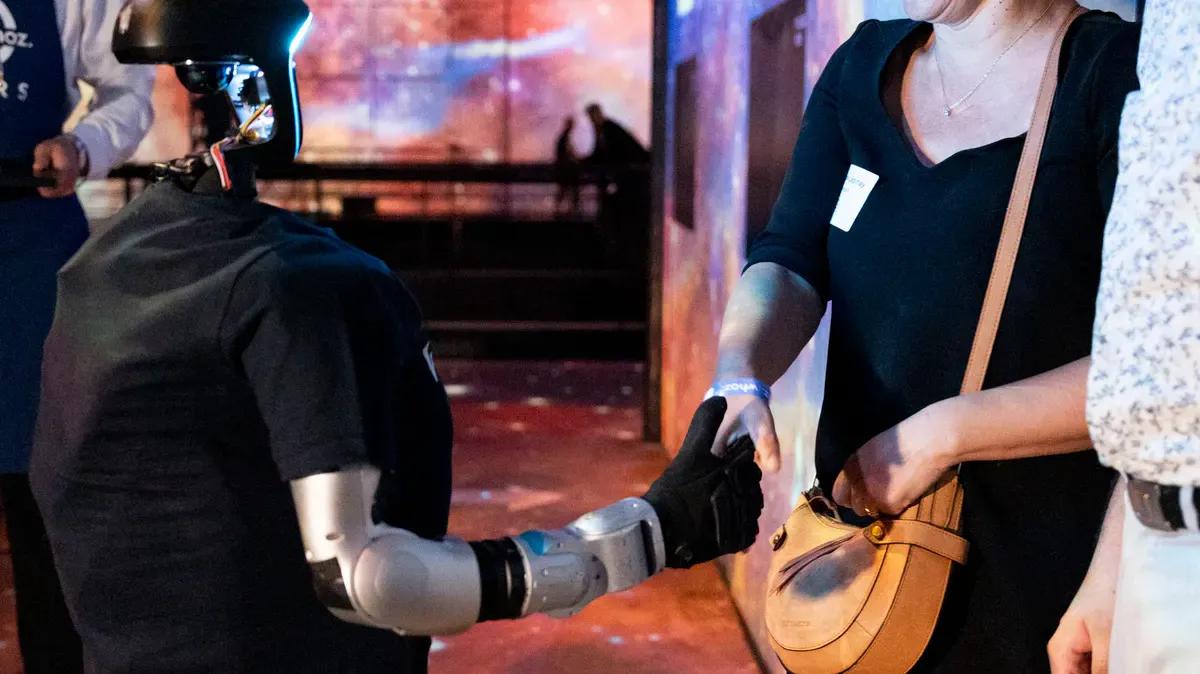 Une invitée serre la main du robot humanoïde Unitree G1 lors d'une soirée d'entreprise à l'Atelier des Lumières, à Paris