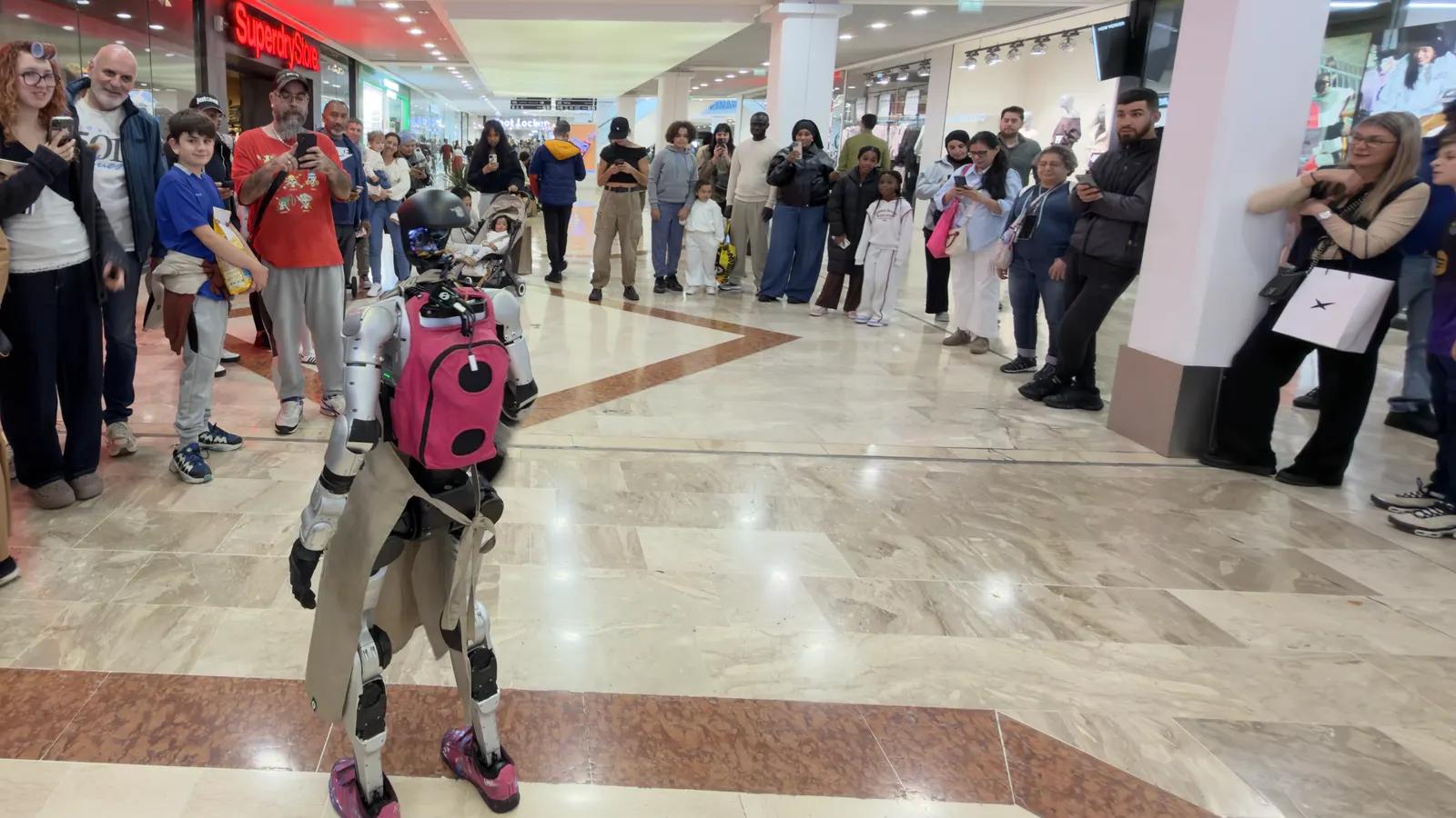 LeoBot avance dans la galerie marchande du centre commercial Belle Épine entre deux haies de visiteurs qui le filment