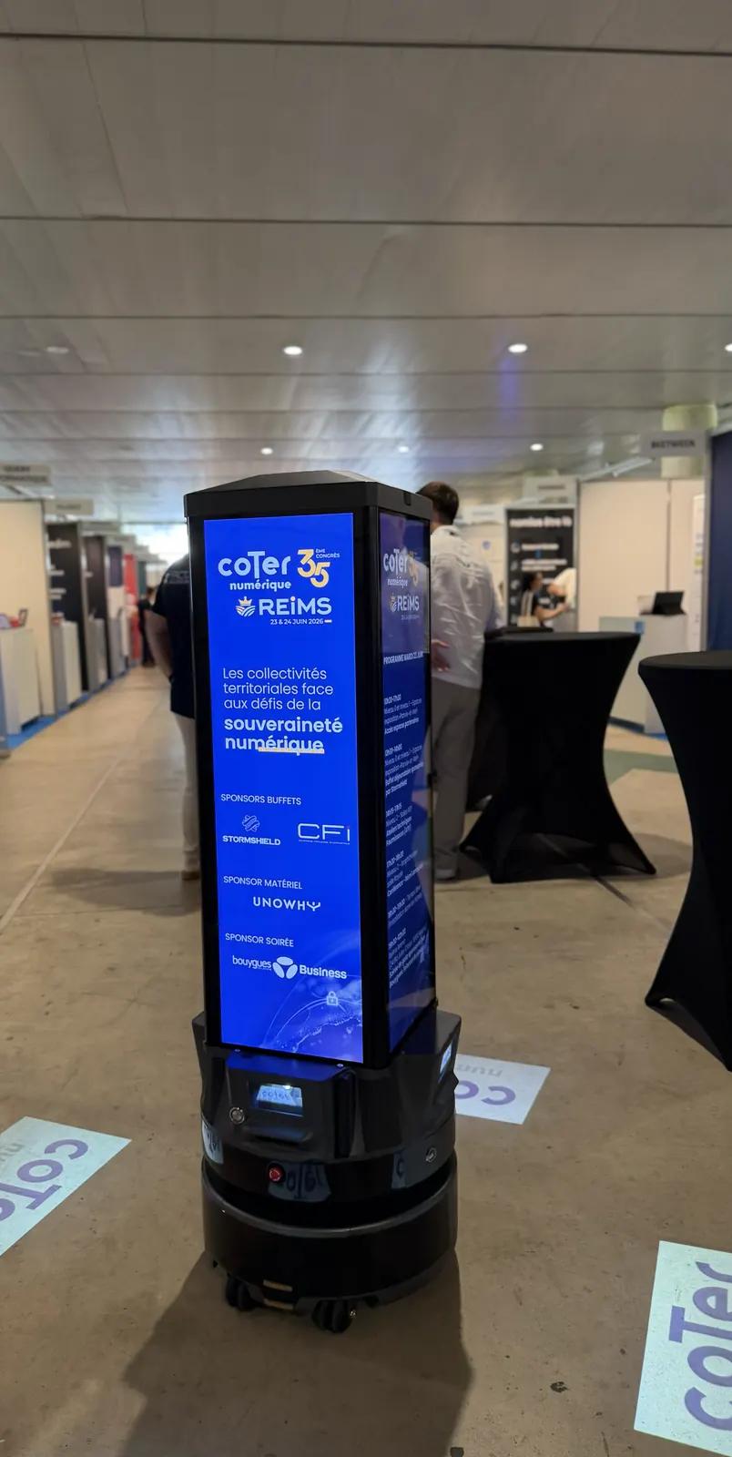 Robot média Fourcast affichant les visuels du congrès sur ses écrans, dans une allée du hall d'exposition à Reims